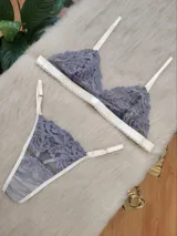 Conjunto de lencería compuesto por un corpiño triangular y una bombacha tipo tanga, confeccionados en encaje gris con detalles de terminaciones en color champagne.
