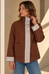 Campera marrón de lino con diseño bicolor, con una franja central gris claro que incluye botones de nácar. Cuenta con cuello alto, mangas largas con puños grises, bolsillos frontales aplicados y silueta amplia.
