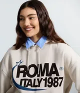 Buzo oversized color beige con capucha ajustable y bolsillo canguro. Presenta un estampado frontal estilo college con el texto "ROMA ITALY 1987" en negro y detalles en azul. Tiene puños y bajo ajustados.