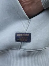 Buzo tipo hoodie de color celeste, confeccionado en tejido fleece, con capucha ajustable mediante cordones y bolsillo frontal tipo canguro.