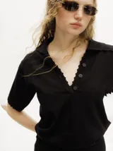 Chomba de punto negro, de manga corta, con cuello tipo polo, escote en V abotonado con detalles de crochet en los bordes y terminaciones acanaladas.