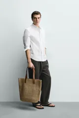 Bolso tipo shopper de acabado trenzado color tostado, con compartimento principal sin cierre, bolsillo plano interior y dos asas de mano de cuero sintético marrón.