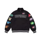 Campera de estilo deportivo con cierre frontal completo y cuello alto. De color negro, presenta el logo de Supreme bordado en el pecho y múltiples parches temáticos de estilo universitario y deportivo en ambas mangas. Incluye puños y ruedo con franjas blancas.