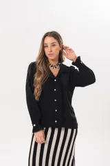 Camisa de manga larga color negro, con cuello camisero, cierre frontal con botones y detalle de volados en la cartera y los puños.