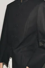 Blazer negro de mezcla de algodón, con cuello subido y manga larga. Cuenta con falsos bolsillos de vivo en el delantero y cierre frontal con alamares a tono.