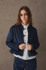 Chaqueta de corte corto y holgado, confeccionada en pana color marrón, con cuello mao, cierre frontal de botones dorados y mangas largas con puños rectos.