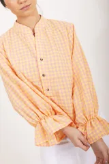 Blusa de diseño cuadrillé en tonos beige y verde claro, de corte amplio y mangas largas abullonadas con puños elastizados con volados. Cuenta con cuello mao y una abertura frontal parcial con botones.