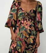 Vestido midi de corte evasé con estampado de follaje tropical sobre fondo negro. Presenta escote corazón, mangas abullonadas y un diseño fluido confeccionado en viscosa.