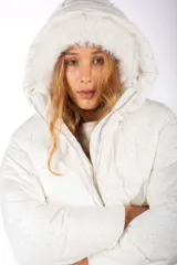 Campera puffer blanca con acabado brillante y pequeños apliques de strass distribuidos por toda la prenda. Cuenta con capucha integrada con borde de piel sintética, cierre frontal metálico y diseño acolchado.