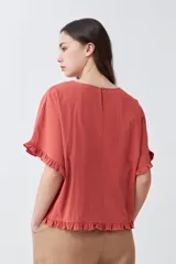 Blusa blanca de corte holgado con cuello redondo, mangas cortas con detalle de volados y ruedo con terminación de volado pequeño.