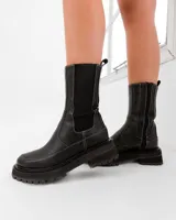 Bota corta de cuero vacuno color negro, con diseño de caña media, elástico lateral y suela de goma tipo track. Cuenta con cierre interno y punta redonda.