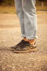 Zapatillas bajas de cuero con estampado animal print, puntera y cordones negros, contrafuerte dorado y suela color caramelo.