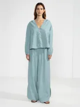 Cardigan abotonado color celeste, confeccionado en lino 100% italiano, con silueta relajada, dobladillo curvado, puños elásticos y un charm floral en el primer botón.