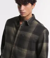 Camisa de manga larga con diseño de cuadros en tonos marrones, confeccionada en algodón. Presenta cuello camisero, cierre frontal con botones y un bolsillo en el pecho con botón.