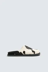 Zueco de piel con pelo con estampado de vaca en blanco y negro. Presenta una horma redonda y una suela de goma negra con volumen.