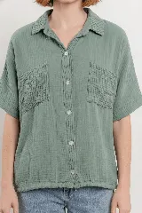 Camisa verde menta de tela arrugada, con cuello clásico, botones frontales, mangas cortas y dos bolsillos delanteros con pespuntes. La base es levemente elastizada y se anuda en el frente.