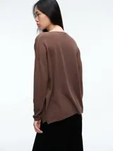 Sweater de punto gris con escote en V profundo, hombros caídos y mangas largas. Presenta un diseño de calce relajado con sutiles micro lentejuelas integradas en el tejido.