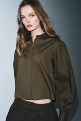 Camisa de popelín color blanco con cuello solapa, cierre frontal con botones ocultos y mangas largas abullonadas con puños estructurados.