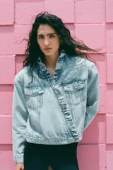 Cazadora de denim color celeste con cuello alto y volantes en el borde frontal. Cuenta con cierre cruzado con botones metálicos y bolsillos en el pecho con solapa.