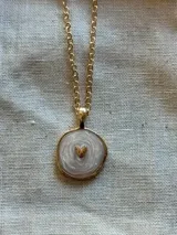 Collar con cadena de eslabones dorados y dije circular con centro de resina marmolada en tonos claros y un pequeño corazón dorado en relieve.