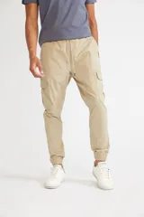 Pantalón cargo color beige con ajuste slim, cintura elástica con cordón ajustable, bolsillos laterales con solapa y velcro, y puños elásticos en los tobillos.