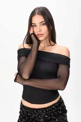 Top negro de manga larga confeccionado en tela semitransparente, con diseño off-shoulder y escote bote drapeado.