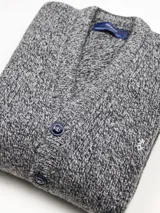 Cardigan de punto grueso con cuello en V y cierre frontal de botones. Presenta un diseño jaspeado en tonos grises y un pequeño bordado en el pecho.