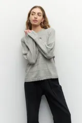 Sweater de tejido de punto color gris melange, con cuello redondo y diseño de franjas horizontales en relieve. Presenta mangas largas acampanadas y un corte holgado.