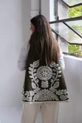 Chaleco abierto de tejido de punto color verde oliva, con bordes decorados con un diseño floral en relieve de color blanco. Presenta una caída fluida y un estilo envolvente.