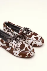 Mocasín tipo boat shoe color marrón, confeccionado en cuero, con cordones de cuero marrón y cordones decorativos azules.