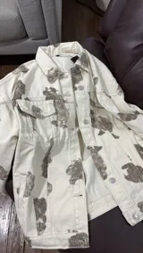 Campera de jean con corte oversize y estampado tipo animal print de manchas en tonos marrones sobre base color crema. Presenta cuello clásico, cierre frontal con botones metálicos, bolsillos con solapa en el pecho y puños abotonados.