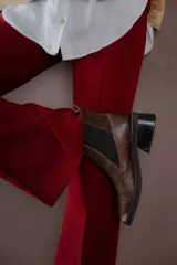 Botas tipo chelsea de cuero color marrón oscuro con acabado brillante. Presentan punta cuadrada con detalle de puntera metálica, elásticos laterales y taco cuadrado bajo.