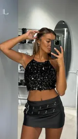 Top corto negro de estilo halter, completamente cubierto de lentejuelas brillantes.