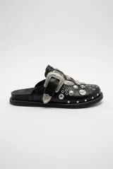 Mocasín de cuero sintético negro con suela plana, detalle de gran hebilla metálica plateada y apliques de tachas y condecoraciones metálicas de estilo western en el empeine.