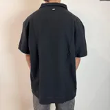 Chomba negra de corte oversize con cuello polo y tapeta de dos botones. Tejido de punto acanalado vertical.