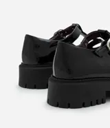 Mocasín estilo Mary Jane de Satinato, confeccionado en poliuretano con acabado brillante. Presenta recortes redondeados en la parte superior, tira ajustable con hebilla metálica y una robusta suela track dentada.