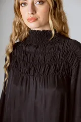 Blusa negra de manga larga con cuello alto fruncido y diseño amplio con frunces en la parte superior.