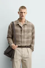 Camisa relaxed fit de manga larga con cuello solapa, confeccionada en tejido con mezcla de viscosa. Presenta un bolsillo plastrón en el pecho, bajo con aberturas laterales y cierre frontal de botonadura. El diseño es a cuadros en tonos beige y marrón.