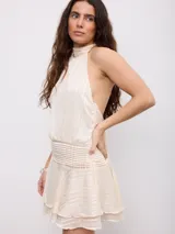 Vestido corto color beige con diseño a rayas sutiles, cuello halter y espalda descubierta. Cuenta con una faja fruncida en la cintura y falda con volados en el borde inferior.
