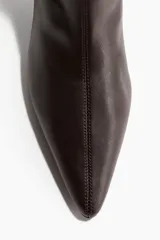 Botines de caña media con diseño entallado, punta fina y costura frontal. Presentan taco fino forrado y cierre lateral.