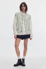 Chaleco oversize de denim color crudo con estampado de lunares negros, cuello camisero, bolsillos delanteros y cierre frontal de botones metálicos.