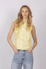 Blusa color amarillo pastel, sin mangas, con cuello camisero y cierre frontal con botones. Presenta volados en los hombros y en el frente.
