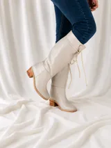 Bota de caña alta color suela, confeccionada en cuero napa, con diseño de caña caída y ajuste mediante cordones en la parte superior. Presenta un taco cuadrado foliado de 4,5 cm y suela de goma antideslizante.