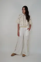 Pantalón de lino blanco con cintura elástica y cordón ajustable, de corte holgado y diseño largo, con detalles de inserciones de malla transparente con bordados florales en los laterales.