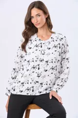 Blusa blanca de manga larga con estampado de hojas pequeñas en gris. Tiene cuello redondo, cierre frontal con botones personalizados y mangas abullonadas con puños elásticos.