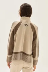 Polera de cuello alto confeccionada en lana lambswool, con diseño de bloques de color en tonos beige y marrón. Presenta mangas raglán con textura acanalada y detalles en hilo metalizado lurex.