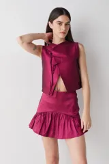 Top sin mangas de estilo cruzado, confeccionado en tela satinada color cobre. Presenta un diseño corto con cierre frontal mediante tiras finas para anudar y cuello redondo.