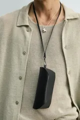 Funda para gafas de cuero negro con acabado abatanado, compartimento con cierre de botón a presión, pasador para cinturón y asa de mano.