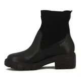 Bota Beira Rio de caña media, color negro, con cuerpo de cuero sintético y caña de tejido elástico acanalado. Cuenta con taco bloque de 4 cm y suela track dentada.
