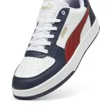 Championes Puma Caven 2.0, color blanco con detalles en azul marino y franja lateral roja. Presenta cordones blancos, perforaciones en la puntera y suela de goma blanca con base azul.